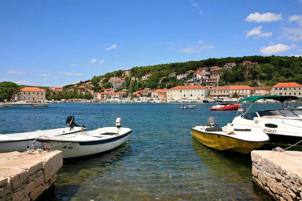 View of Jelsa harbor on Hvar Island, Croatia, with small boats docked and hillside houses in the background under a clear blue sky