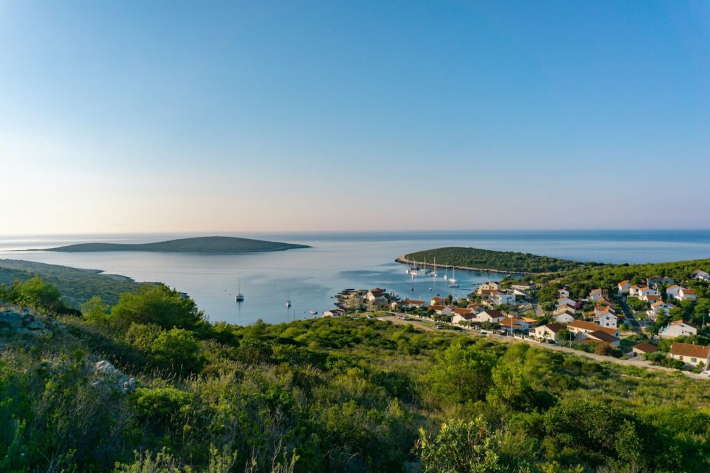 View of a peaceful fishing village on Vis Island, Croatia, with sailboats in a calm bay and green hills surrounding the coast