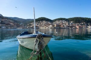 Moored boat in the calm turquoise bay of Pučišća on Brač island, Croatia, with traditional stone houses and a church tower rising along the hillside in the background.